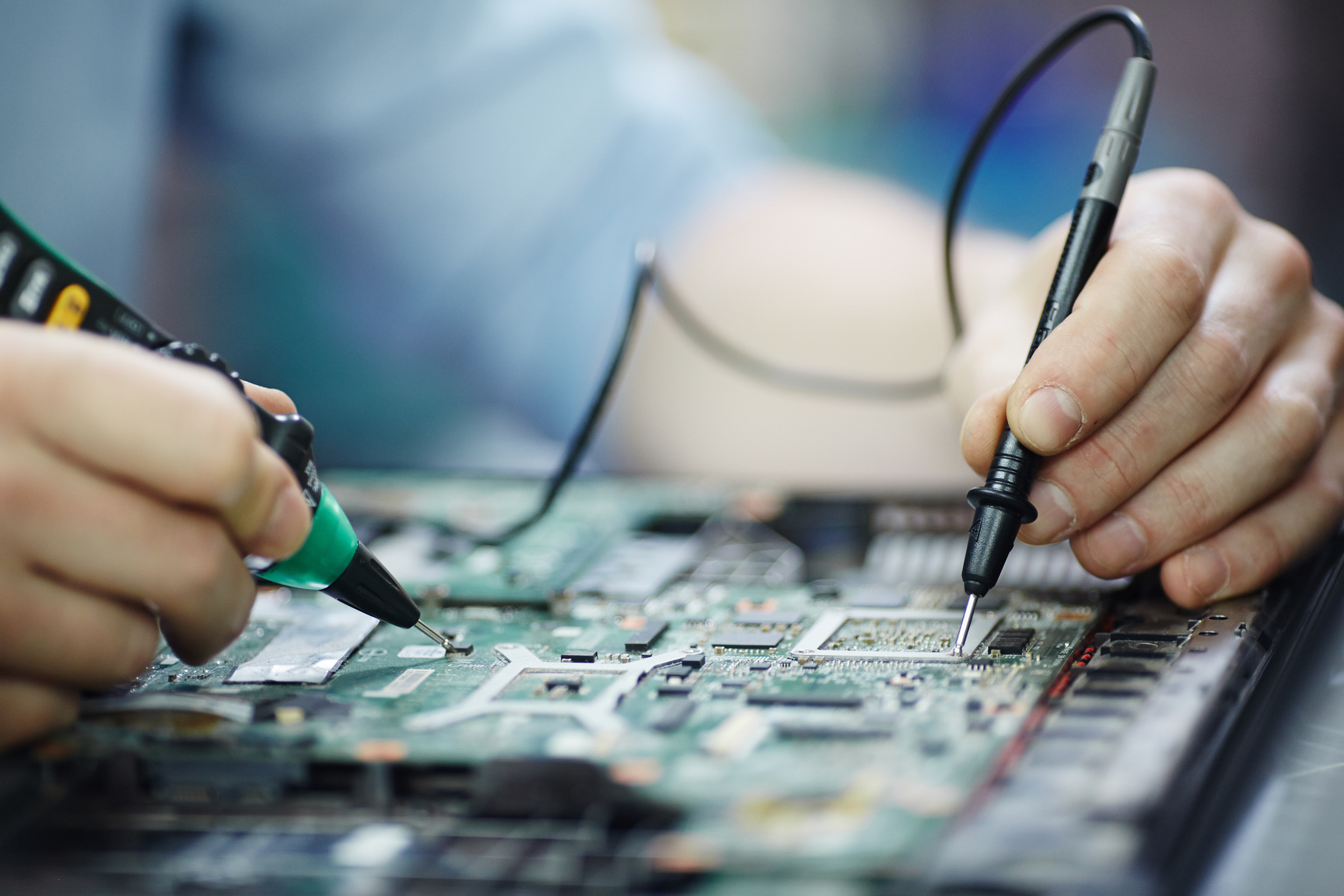 technician checking voltage, resistance to ground on laptop motherboard using multimeter probes